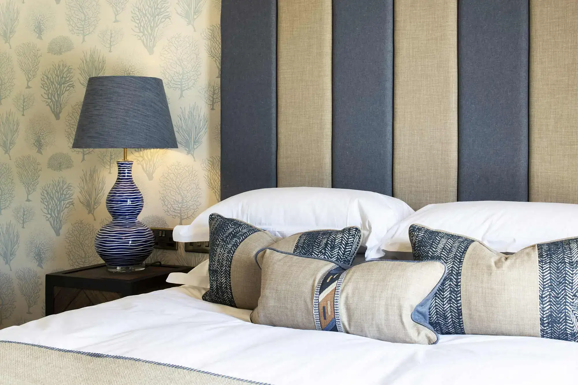 Bed with a lamp behind tree-patterned wallpaper